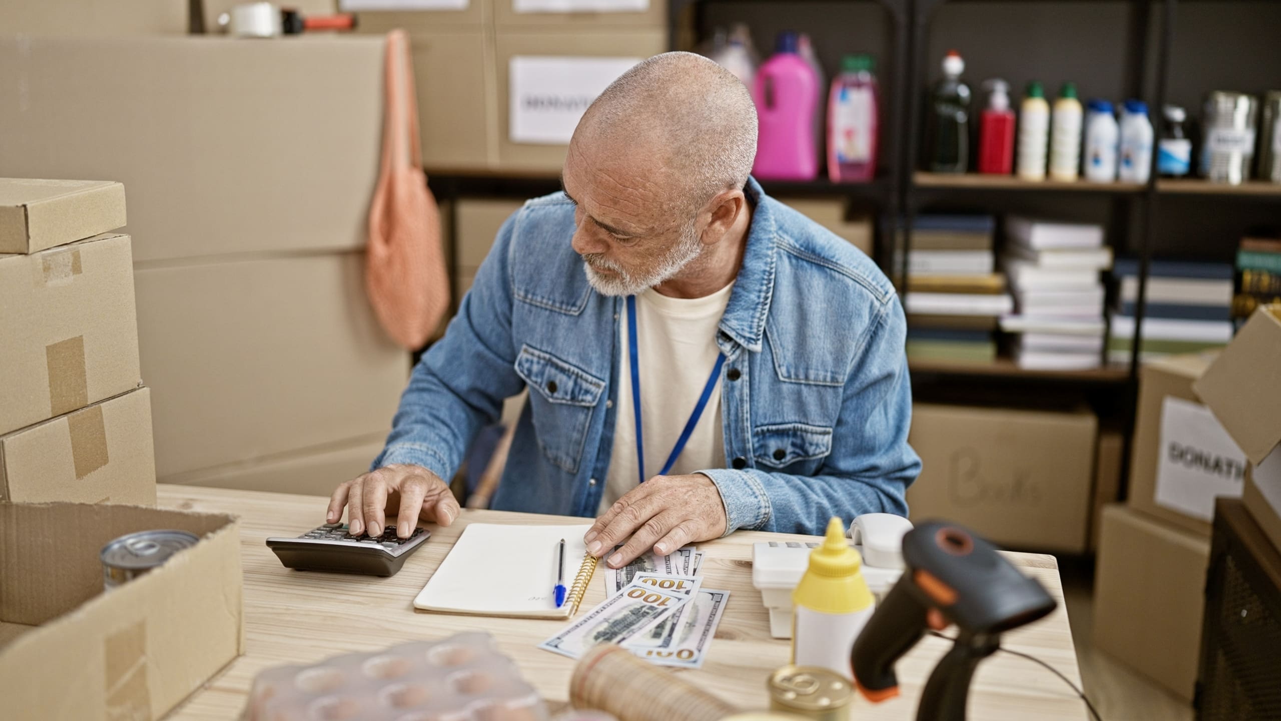 A man works on bills in backroom with boxes.